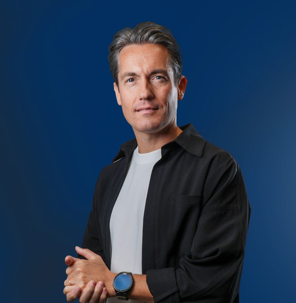 Man met blauwe achtergrond en zwarte blouse.